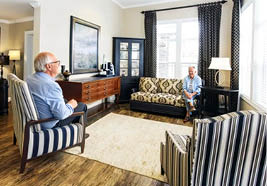 A man sitting in a chair with a striped couch in the background. Description generated by AI
